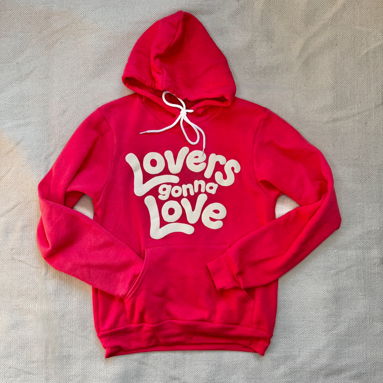 An bright red hoodie that reads Lovers Gonna Love